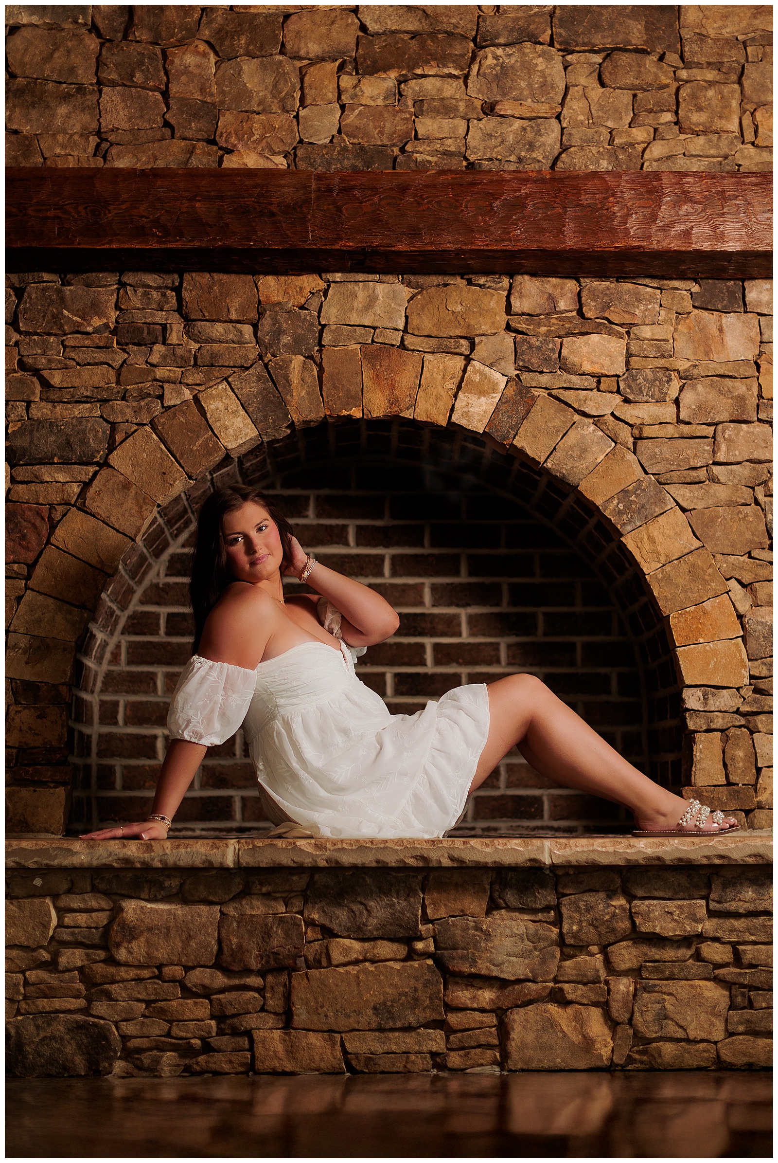 Senior girl pictures in white dress at stone fireplace at The Farmer’s Daughter at Walston Pond in North Carolina.
